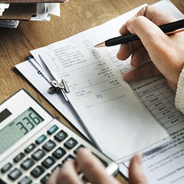 Person writing notes on clipboard with financial documents